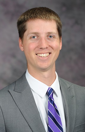 Daniel Skucius, wearing a grey suit and purple tie, poses for a photograph.