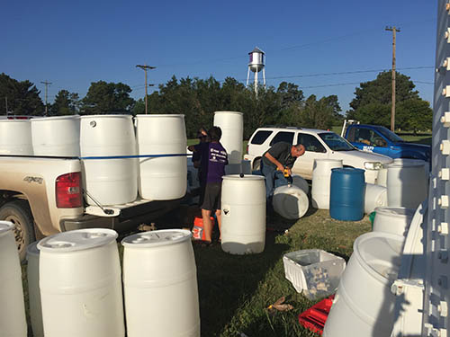 Large white plastic barrels are prepared for use as rain barrels