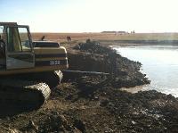 A digger begins digging the trench into the front of the pond dam.