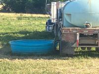This photo shows a view of a water truck that is pumping into a plastic livestock watering tank.