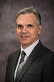 Aleksey Sheshukov, wearing a suit and tie, smiles at the camera in this formal portrait