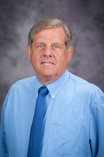 Steve Ensley, in a blue shirt and tie, smiles at the camera