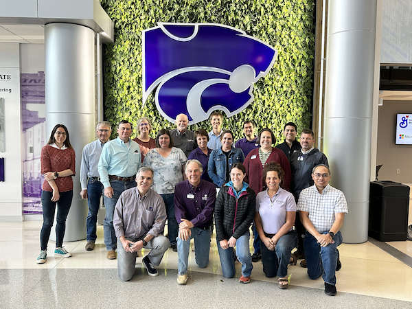 A group of people pose together in front of a living green wall with a large purple powercat sign