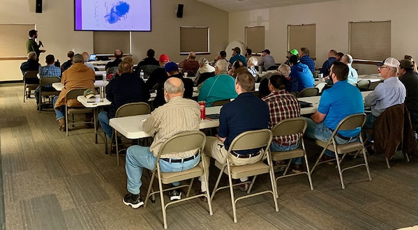 a group of people are seated in a large room, listening to a presentation
