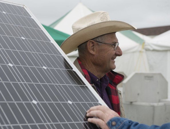 Hershel George, wearing a hat and smiling at someone off camera, stands in front of a solar panel.