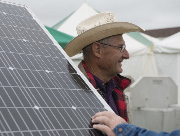 Herschel George, wearing a hat, stands next to a solar panel