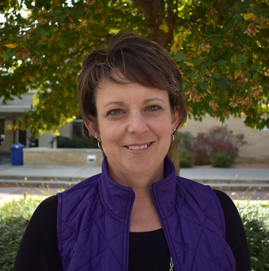 Stacie Minson, standing in front of a tree with green foliage, smiles at the camera