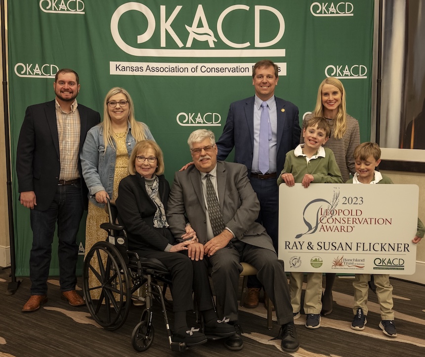 The Flickner family stands in front of the green KACD banner, holding their Leopold Conservation Award sign